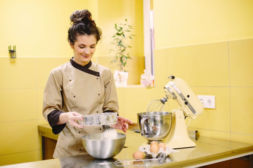 Woman preparing pastries. Confectioner in a coat. Woman on a yellow background.