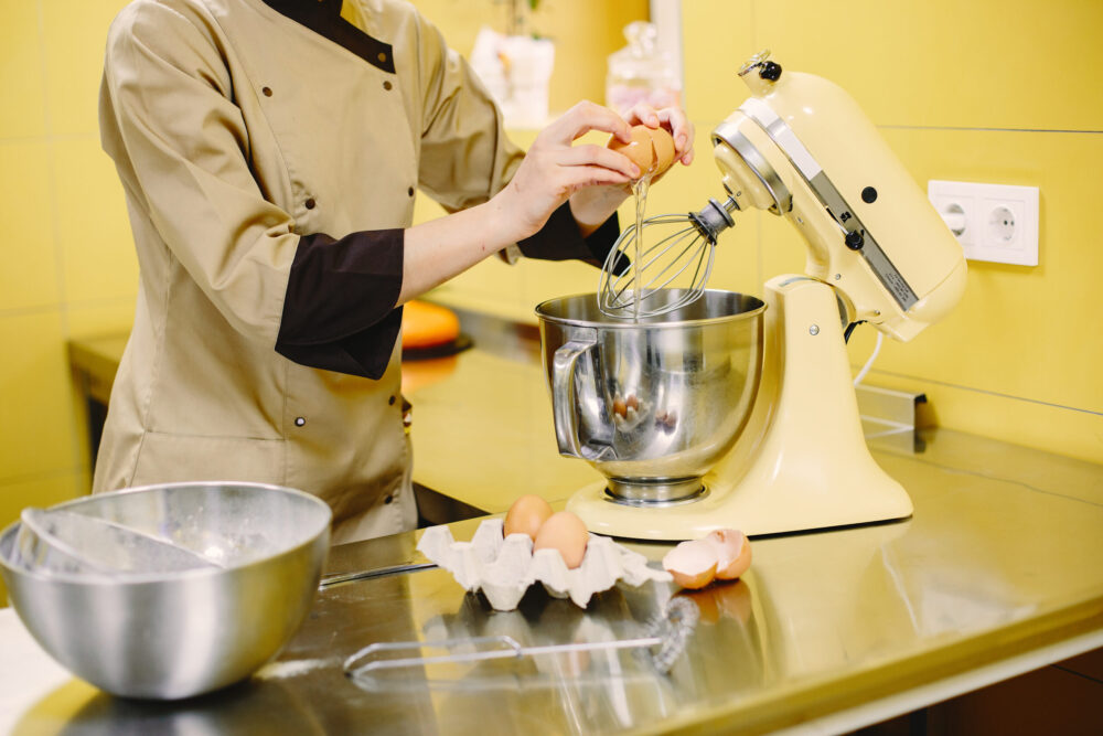 Woman preparing pastries. Confectioner in a coat. Woman on a yellow background.