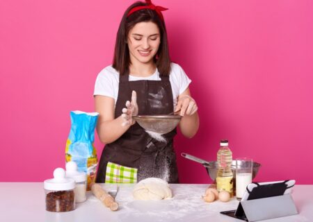 portrait-skillful-talented-cook-putting-flour-through-sieve-half-ready-pie-with-raisin-brunette-cute-young-model-poses-isolated-bright-pink-baking-cooking-concept_176532-8425